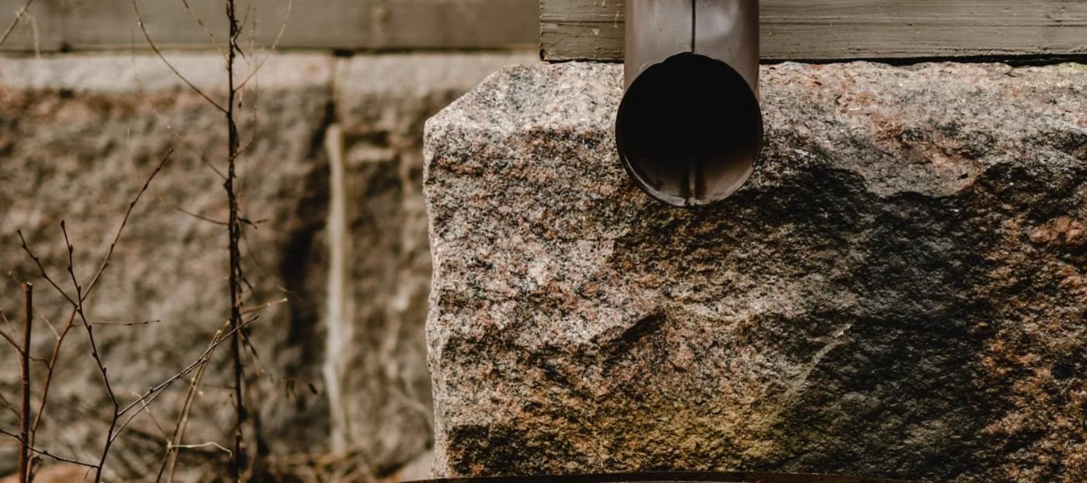 Metal downspout ending at the stone foundation of an older house
