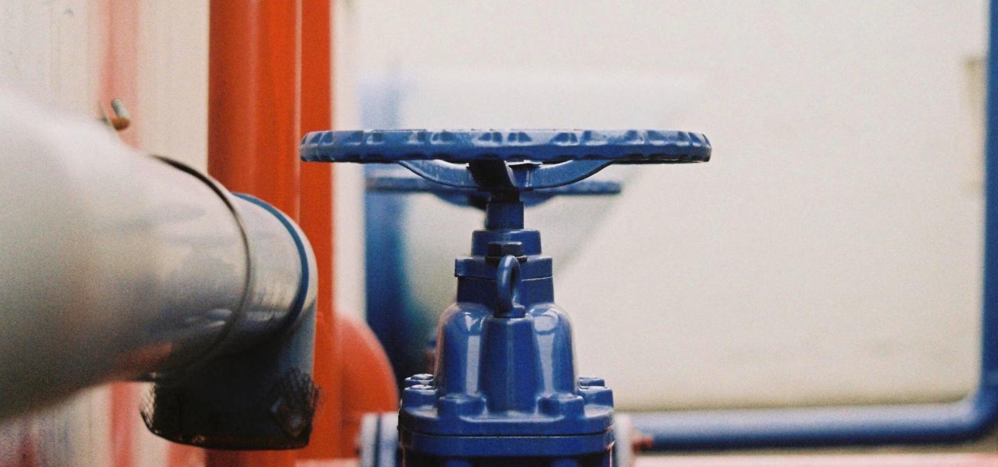 Close-up of a blue wheel-handle gate valve on a water line, with gray and orange pipes blurred in the background