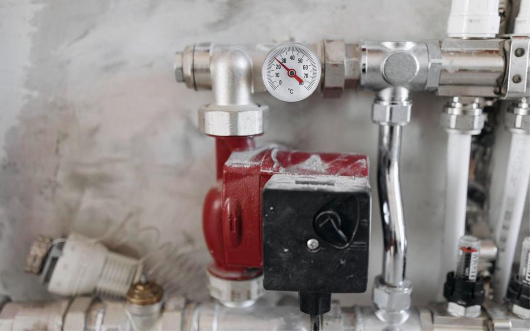 Close view of a red hot water circulating pump, a temperature gauge and chrome pipe fittings mounted on a utility room wall